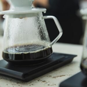 Glass coffee pot with fresh brew on digital scale, capturing modern café vibe.